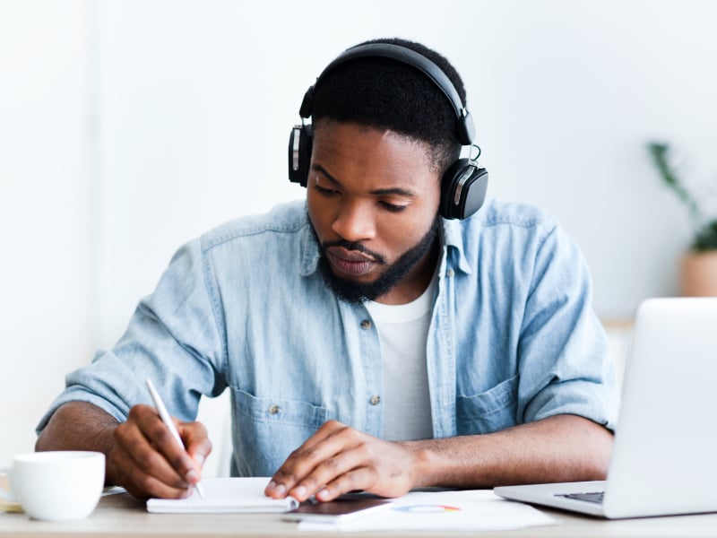 young man studying, wears headphones, drinks coffee